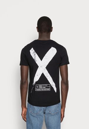Schwarzes Baumwoll-T-Shirt mit großem weißem Kreuz-Design auf der Rückseite, begleitet von Text in einem rechteckigen Etikett unten.