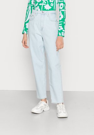 Person wearing light blue high-waist straight jeans, green long-sleeve top with white floral pattern, and white chunky sneakers.