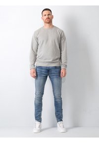 Hanorac gri cu decolteu rotund și manșete fasonate, asociat cu blugi skinny de un albastru deschis. Tenisi albi completează ținuta.