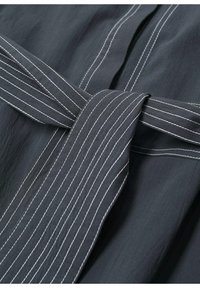 Tissu gris foncé à surface texturée, avec une large ceinture à rayures blanches nouée à la taille et un devant boutonné.