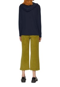 Marineblauer Kapuzenpullover mit Kapuze, kombiniert mit grünen Wildleder-Hosen im weiten Schnitt. Das Model trägt schwarze glänzende Schuhe. Die Rückansicht zeigt ein einfaches Design und eine ansprechende Textur.