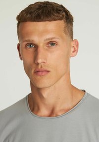 Grijze crewneck t-shirt op een mannelijke model, met korte mouwen en een gladde textuur, met een eenvoudig ontwerp en zachte, gedempte kleur.