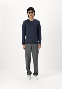 Jersey de punto azul marino con cuello redondo y mangas largas, combinado con pantalones gris claro y zapatillas blancas. Gafas de sol redondas realzan el look.