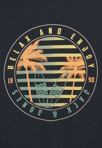 Camiseta azul oscuro con un gráfico circular que incluye palmeras, tablas de surf y texto en colores pastel. Fondo a rayas en amarillo y verde.