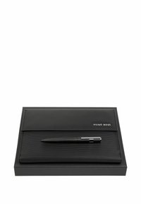 Pochette à documents en cuir noir de marque Hugo Boss et stylo noir posés sur une boîte noire sur fond blanc.
