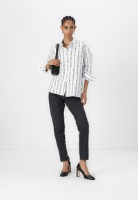 Hvit skjorte med svarte vertikale striper og sirkulære detaljer, kombinert med mørke jeans og svarte hæler. Inkluderer en liten svart veske.