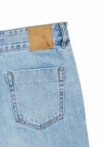 Pantalones vaqueros de mezclilla azul claro con un parche cuadrado de cuero marrón en la cintura y un único bolsillo trasero con forma puntiaguda.