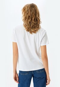 Hvid bomulds t-shirt med korte ærmer, en afslappet pasform og rund halsudskæring, parret med blå denim jeans. Ingen synlige logoer eller mønstre.