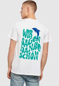 Hvid bomulds t-shirt med turkise bogstaver "WIR SAGEN DANKE SCHÖN" og et blåt delfin grafik på ryggen. Korte ærmer, afslappet pasform.