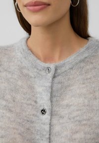 Szary dzianinowy kardigan z okrągłym dekoltem, cechujący się miękką, puszystą fakturą i jednym błyszczącym zapięciem na guzik u dekoltu.