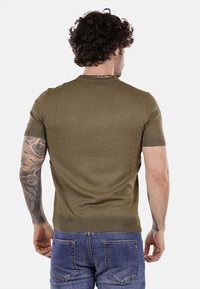 Maglione verde oliva a maniche corte dal design aderente, realizzato in materiale a coste, con scollatura rotonda e cuciture laterali.