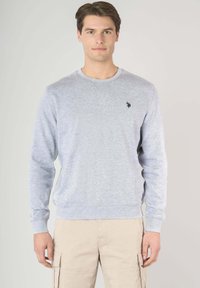 Felpa grigia chiara in un tessuto morbido con maniche lunghe, collo a giro e un piccolo logo nero sul lato sinistro del petto. Abbinala a pantaloni cargo beige.