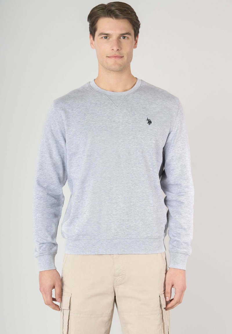 Felpa grigia chiara in un tessuto morbido con maniche lunghe, collo a giro e un piccolo logo nero sul lato sinistro del petto. Abbinala a pantaloni cargo beige.