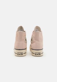 Para różowych trampek Converse All Star w stylu wysokim, widok z tyłu, pokazujący łatki z logo oraz beżowe gumowe podeszwy z czarnymi paskami.