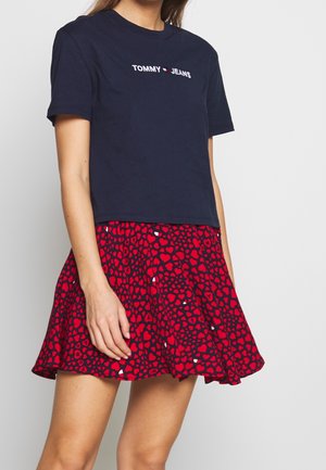 Mørkeblå bomulds t-shirt med "TOMMY JEANS" logo; parret med et rødt nederdel dækket af hjerte mønstre og en udvidet design.