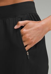 Black athletic shorts with textured fabric and an elastic waistband, featuring a zippered pocket at the side. Hand in pocket for scale.