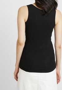 Top a canottiera nera a coste con un design aderente. Presenta spalline larghe e un collo arrotondato. Si vede un abbinamento con una gonna bianca.