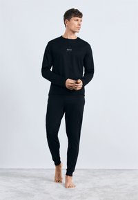 Sudadera de manga larga negra y pantalones a juego, confeccionados con una tela suave. Presenta un sutil logo "BOSS" en el pecho. Ajuste ceñido.