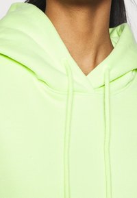 Felpa in cotone verde neon con cappuccio regolabile, texture morbida e vestibilità comoda, che mostra i dettagli del tessuto e delle cuciture.