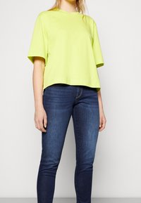 Camiseta de algodón de gran tamaño en verde lima, con mangas cortas y un dobladillo recto, emparejada con jeans ajustados azul oscuro. Textura suave, ajuste casual.