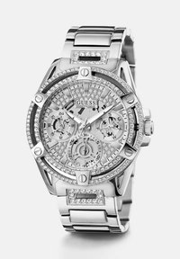 Srebrna ura iz nerjavečega jekla z kristalnimi detajli in kronografskim zaslonom. Ima okroglo številčnico in zasnovo zapestnice iz sedežnih povezav. Model: Guess.