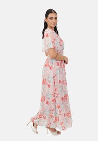 Robe maxi florale en tissu léger, rose, ornée de fleurs rouges et turquoises. Dotée de courtes manches flottantes et d'une taille cintrée pour un ajustement fluide.