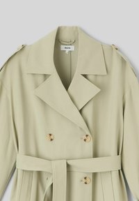 Manteau trench double boutonnage vert clair avec grands revers, boutons dorés et une ceinture en tissu assortie. Texture lisse et design ajusté.