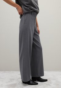 Grijze wijde broek van een zachte stof, met voorzakken, een op maat gemaakte tailleband en gecombineerd met slanke zwarte enkellaarsjes.