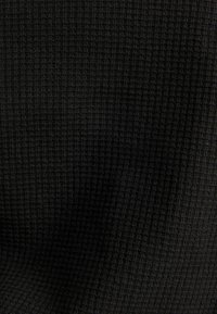 Černá texturovaná tkanina s malým opakujícím se vaflovým vzorem rovnoměrně rozloženým po celé ploše.