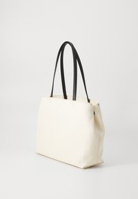 Sac en toile crème avec des poignées en cuir noir. Présente une forme structurée, un design minimaliste et des détails de couture discrets.