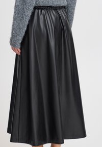 Schwarzer Leder-Midi-Rock mit elastischem Bund, der eine glatte Textur und eine fließende Silhouette aufweist, kombiniert mit einem grauen, flauschigen Pullover.