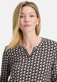 Bluzka we wzory z dekoltem w kształcie litery V, czarno-różowym geometrycznym wzorem i długimi rękawami. Wykonana z lekkiego materiału o gładkiej fakturze.