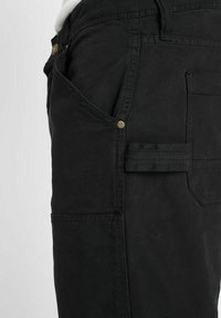 Zwarte cargobroek met een gestructureerde pasvorm, zijzakken en een zichtbaar messing knoopaccent. Gemaakt van duurzame, gestructureerde stof.