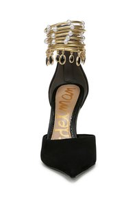 Tacco a punta in suede nero con una cavigliera in oro e perle adornata con charm, che crea un design elegante a strati.