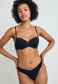 Black lingerie set featuring a padded balconette bra with adjustable straps and a matching low-rise thong. Smooth texture, minimalist design.