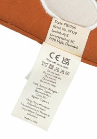 Etiqueta de tela marrón con instrucciones de cuidado y detalles de composición. Incluye información sobre algodón orgánico y espuma de poliuretano. Fabricado en India.