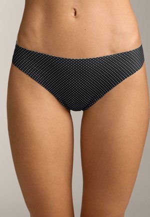 Chiloti de bikini negri cu mici buline albe, purtați de o persoană, arătând talia, șoldurile și părțile superioare ale coapselor pe un fundal neutru.