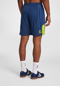 Marina sportshorts med en grön accent på sidan, med resårmidja och en logotyp. Bärs med vita ankelsockor och marina skor.