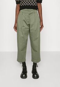 Olivgrön, vida byxor med framtill veck och hög midja, matchade med svarta snörboots. Slät tygtextur, skräddarsydd design.