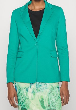 Teal kavaj med slag, enkel knappstängning, framfickor och en figursydd design, kombinerad med en svart topp och mönstrad kjol.