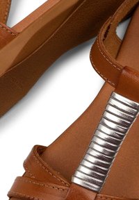 Brown leather sandals with a textured interior, featuring a silver metallic accent on the strap, and a wide, flat sole for comfort.
