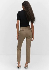 Zwarte top met korte mouwen, gecombineerd met aansluitende bruine geruite broek. Bevat smalle benen en twee achterzakken. Ggedragen met zilveren enkelsandalen.