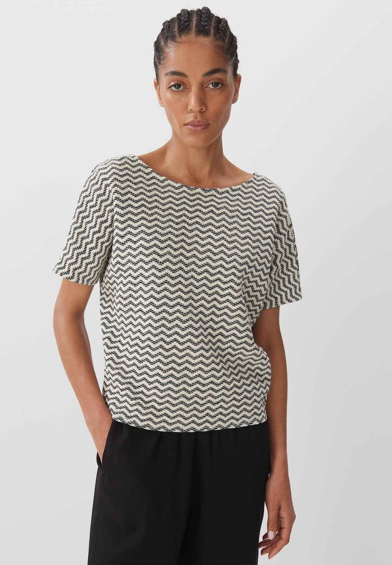 T-shirt à manches courtes en crème avec un motif zigzag noir. Coupe décontractée avec un large col, fabriqué à partir d'un tissu texturé.