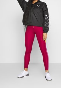 Svart jacka med vit logotyp och grafik, matchad med tajta magentaröda leggings med gula och rosa sidopaneler, avslutade med vita sneakers.