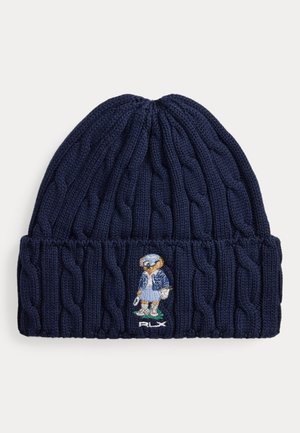 Bonnet bleu marine en maille torsadée avec bord replié, orné d’un ours brodé vêtu de vêtements d’hiver et logo RLX blanc en dessous.