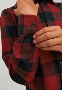 Röd och svart rutiga flanellskjorta med långa ärmar, knapprad vid manschetten och ett mjukt, texturerat tyg.