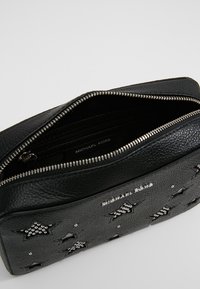 Clutch in pelle nera con decorazioni a motivo stellato, chiusura con zip e dettagli in argento. Presenta un interno con marchio e superficie testurizzata.