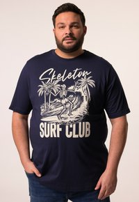 Camiseta de algodón azul marino con un gráfico de un esqueleto surfeando y palmeras, con el texto "Skeleton Surf Club" en blanco. Mangas cortas y corte holgado.