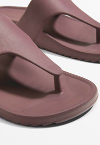 Sandelă flip-flop texturată, de culoare mov, cu design tip thong și talpă plată. Dispune de un suport central pentru degetul mare și material neted, durabil.