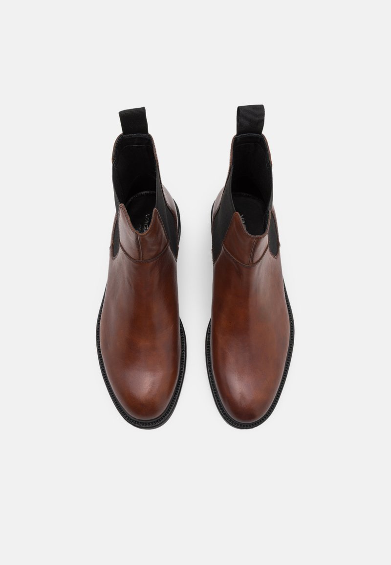 Bruna läder Chelsea-boots med en slät yta, elastiska sidopaneler och öglor för enkel påtagning, satta på en strukturerad svart sula.